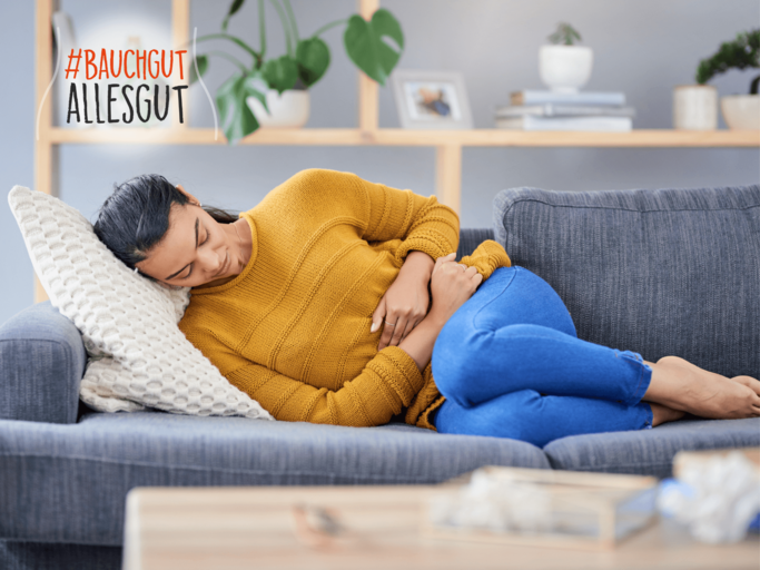 Frau liegt mit Bauchschmerzen auf dem Sofa | © Getty Images/LaylaBird
