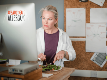 Frau nimmt ihr Mittagessen am Schreibtisch vor dem Computer ein. | © SolStock/iStock