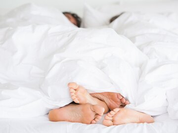 Mann und Frau liegen unter der Bettdecke und die nackten Füße sind zu sehen | © gettyimages.de / Tom Merton