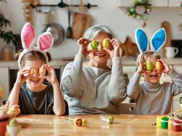 Frau und zwei Kinder halten sich bemalte Ostereier vor die Augen | © AdobeStock/JenkoAtaman