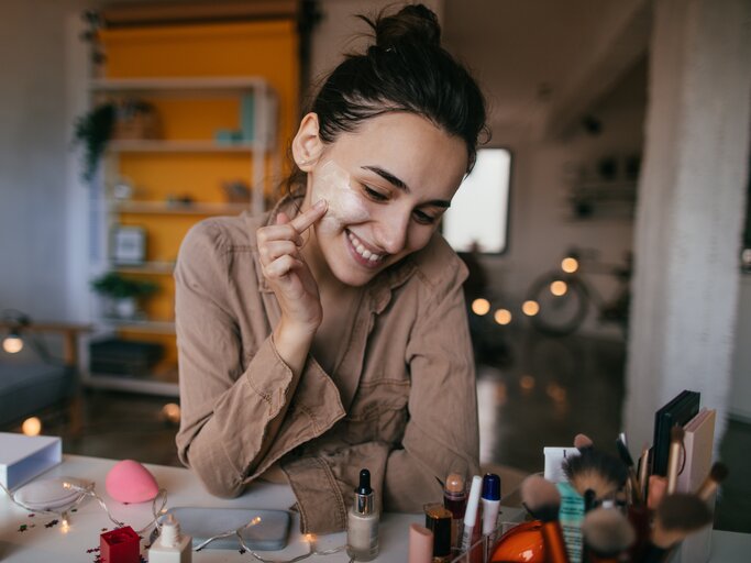 Frau sitzt am Schminktisch und blickt auf ihre Beauty-Produkte | © Getty Images/	AleksandarNakic