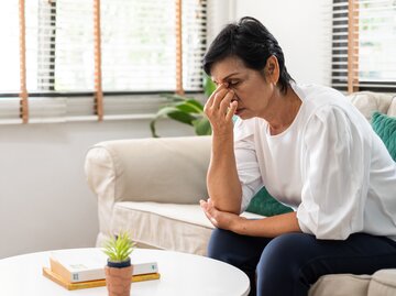 Frau sitzt müde auf der Couch, weil sie in den Wechseljahren ist | © Getty Images/Nattakorn Maneerat