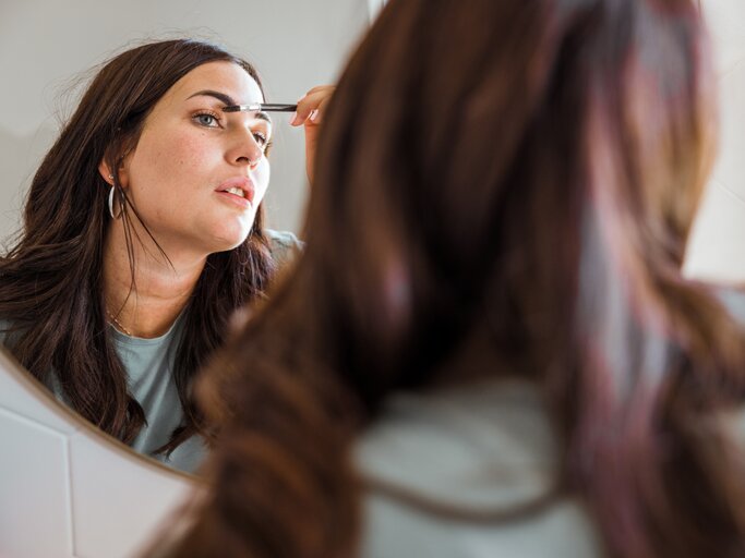 Frau schminkt sich ihre Augenbrauen im Spiegel | © Getty Images/	LeoPatrizi