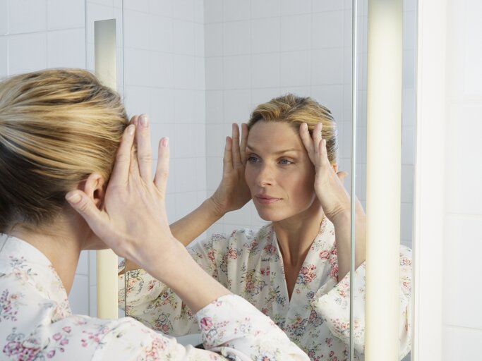 Frau blickt prüfend in den Spiegel | © Getty Images/	Robert Decelis