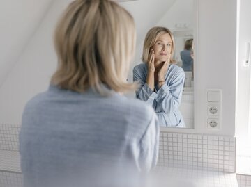 Reife Frau blickt in den Spiegel | © Getty Images/	Westend61