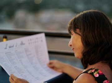 Frau sitzt im Restaurant und studiert das Menü | © Getty Images/	aire images