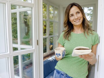 Frau hält Buch in einer und Kaffee in anderer Hand | © Getty Images/Westend61