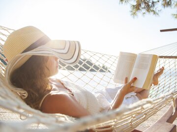 Frau liegt in einer Hängematte und liest ein Buch | © GettyImages/	eternalcreative
