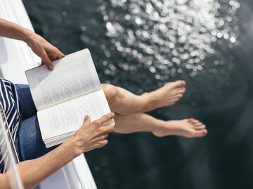 Frau sitzt am See und liest ein Buch | © Getty Images/Westend61