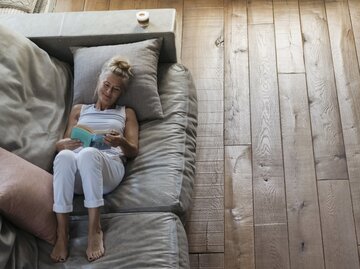 Frau liest entspannt auf der Couch ein Buch | © Getty Images/	Westend61