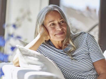 Reife Frau sitzt entspannt auf dem Sofa und lächelt | © Getty Images/Westend61