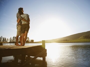 Paar steht am See zum Sonnenuntergang | © Getty Images/	Tom Merton