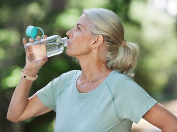 Reife Frau trinkt im Freien aus einer Wasserflasche | © Getty Images/PeopleImages