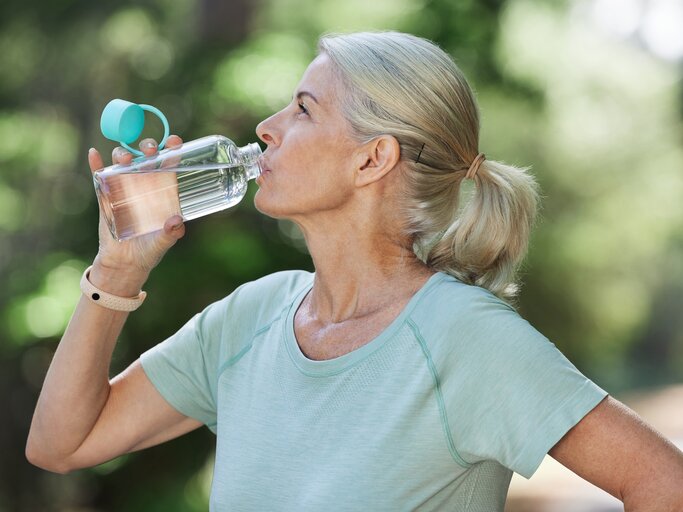 Reife Frau trinkt im Freien aus einer Wasserflasche | © Getty Images/PeopleImages