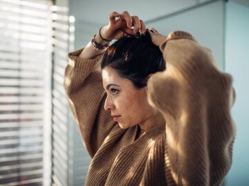 Frau bindet sich Dutt im Badezimmer | © Getty Images/AleksandarNakic