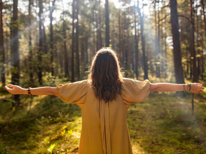 Frau steht mit offenen Armen im Wald | © AdobeStock/Syda Productions