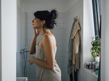 Frau steht im Bad nach einer Dusche | © GettyImages/FreshSplash