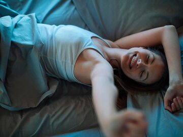 Frau streckt sich im Bett und lächelt | © AdobeStock/Geber86
