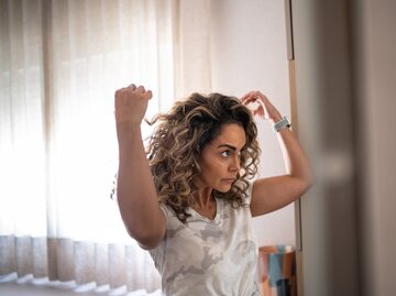 Erwachsene Frau um die 50 blickt prüfend in den Spiegel | © GettyImages/FG Trade