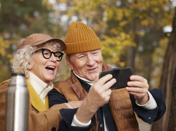 Senioren-Paar hat Spaß beim Fotografieren im herbstlichen Wald | © GettyImages/Johner Images