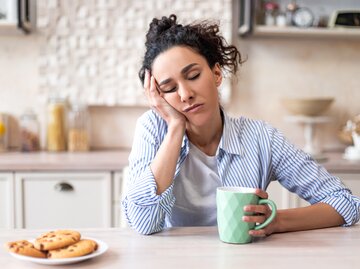 Müde Frau sitzt mit Kaffe am Tisch | © AdobeStock/Prostock-studio