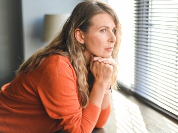 Frau blickt nachdenklich aus dem Fenster | © GettyImages/	elenaleonova