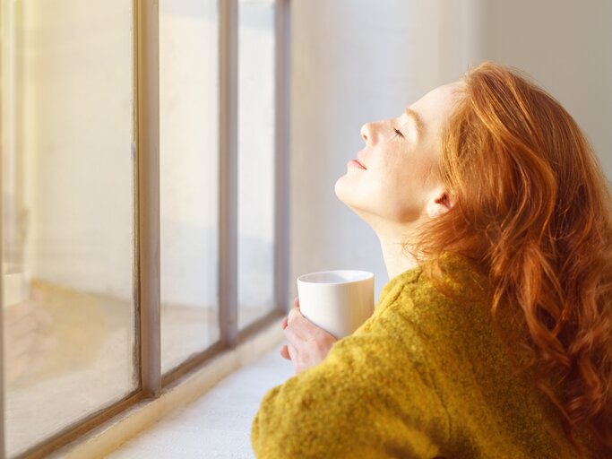 Frau blickt glücklich aus dem Fenster | © AdobeStock/contrastwerkstatt