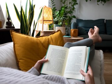 Frau liegt auf dem Sofa und liest ein Buch | © GettyImages/Daniel