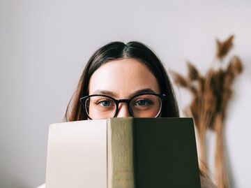 Frau mit Brille liest ein Buch über Psychologie | © GettyImages/nikkimeel