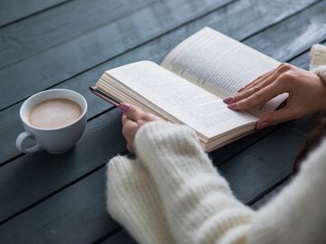 Frau liest Buch und trinkt einen Kaffee | © AdobeStock/Daniel