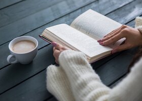 Frau liest Buch und trinkt einen Kaffee