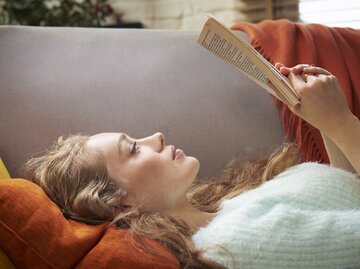 Frau liest Buch auf der Couch | © GettyImages/	Tara Moore