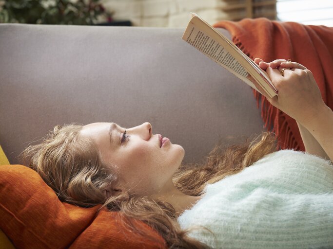 Frau liest Buch auf der Couch | © GettyImages/	Tara Moore