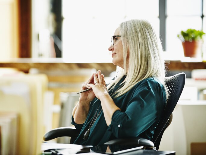 Frau sitzt im Bürostuhl und denkt nach | © GettyImages/ThomasBrawick