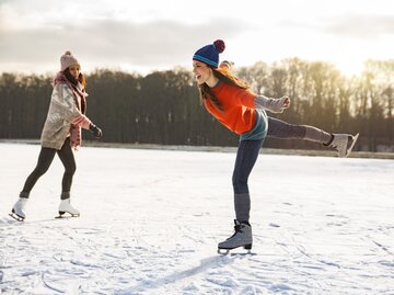 Zwei junge Frauen beim Schlittschuhlaufen im Winter | © Getty Images/	Westend61