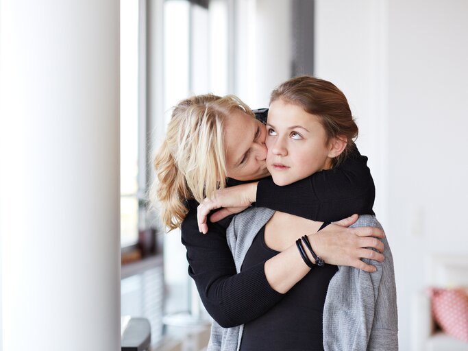 Eine Mutter umarmt ihre Tochter von hinten und diese schaut genervt | © GettyImages/Klaus Vedfelt