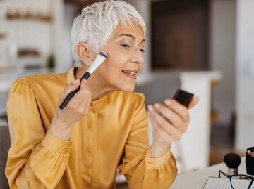 Frau mit grauen Haaren schminkt sich mit einem Pinsel | © Getty Images/milan2099