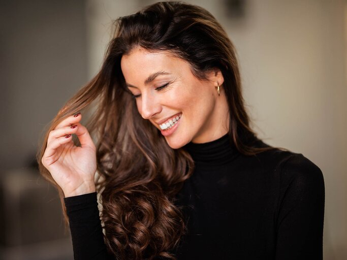 Lächelnde Frau mit lockigem, braunem Haar | © AdobeStock/gzorgz