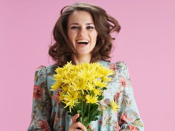 Porträt einer Frau mit fliegenden, langen, braunen Haaren und mit einem gelben Frühlingsstrauß in den Händen | © Getty Images / CentralITAlliance