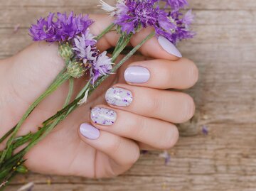 Nahaufnahme von fliederfarbenen Nägel mit Blumenmotiv. | © Getty Images / DevMarya