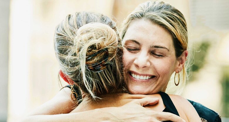 Lachende, blonde Frau umarmt blonde Frau mit Dutt | © Getty Images/Thomas Barwick
