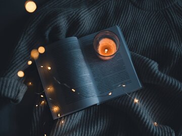 Buch mit Kerze und Lichterkette | © Getty Images/morrowlight