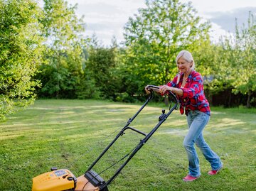 Frau in kariertem Hemd und Jeans mäht den Rasen | © AdobeStock/Halfpoint