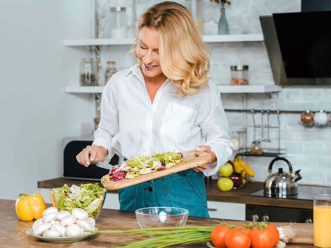 Schöne reife Frau bereitet sich einen gesunden Salat in einer modernen Küche | © iStock | LightFieldStudios