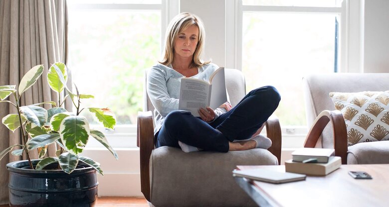 Frau sitzt auf einem Sessel und liest Buch | © iStock/Stígur Már Karlsson /Heimsmyndir