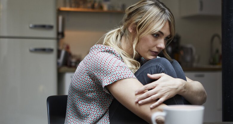 Nachdenkliche Frau sitzt mit angewinkelten Beinen in der Küche | © Getty Images/	Westend61