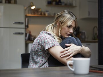 Nachdenkliche Frau sitzt mit angewinkelten Beinen in der Küche | © Getty Images/	Westend61