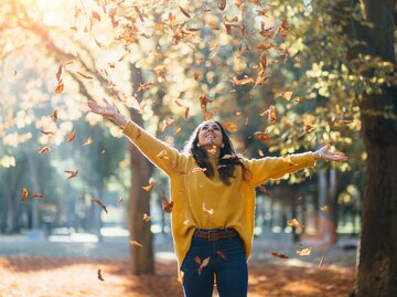 Frau wirbelt Herbstlaub auf | © AdobeStock